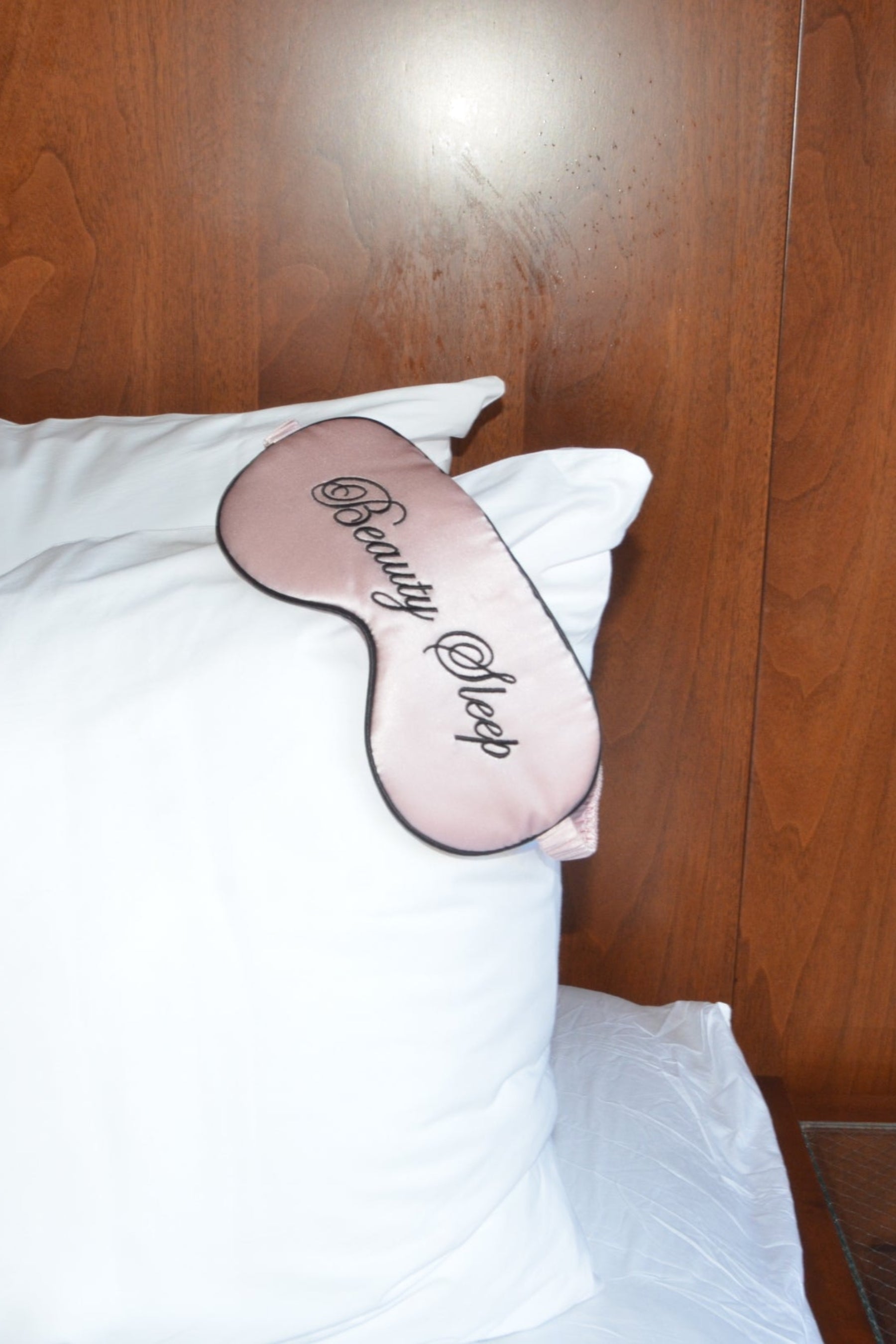 Sleep mask on a pillow with wooden headboard and nightstand in the background
