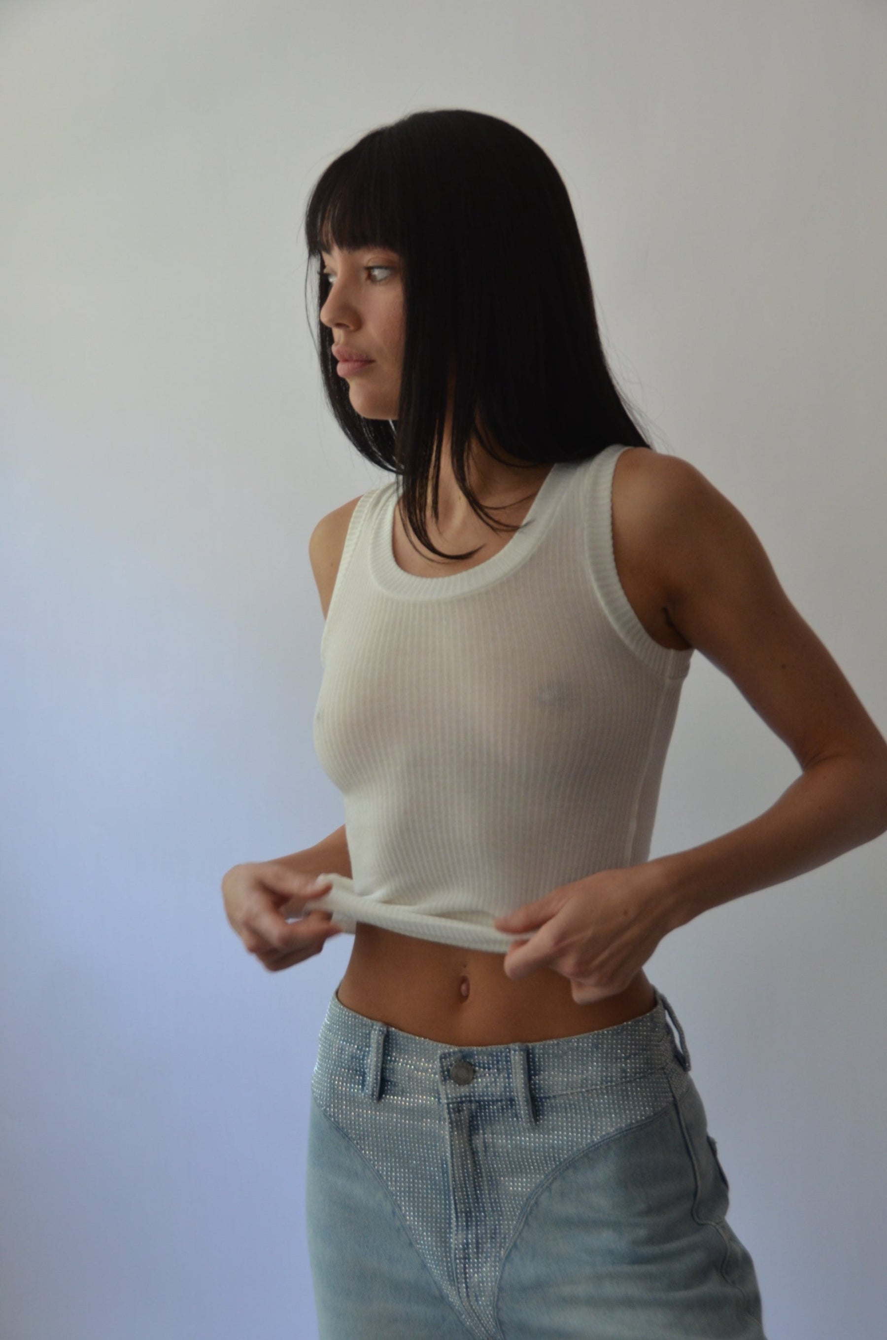 Woman wearing a white sleeveless top and denim shorts against a plain background