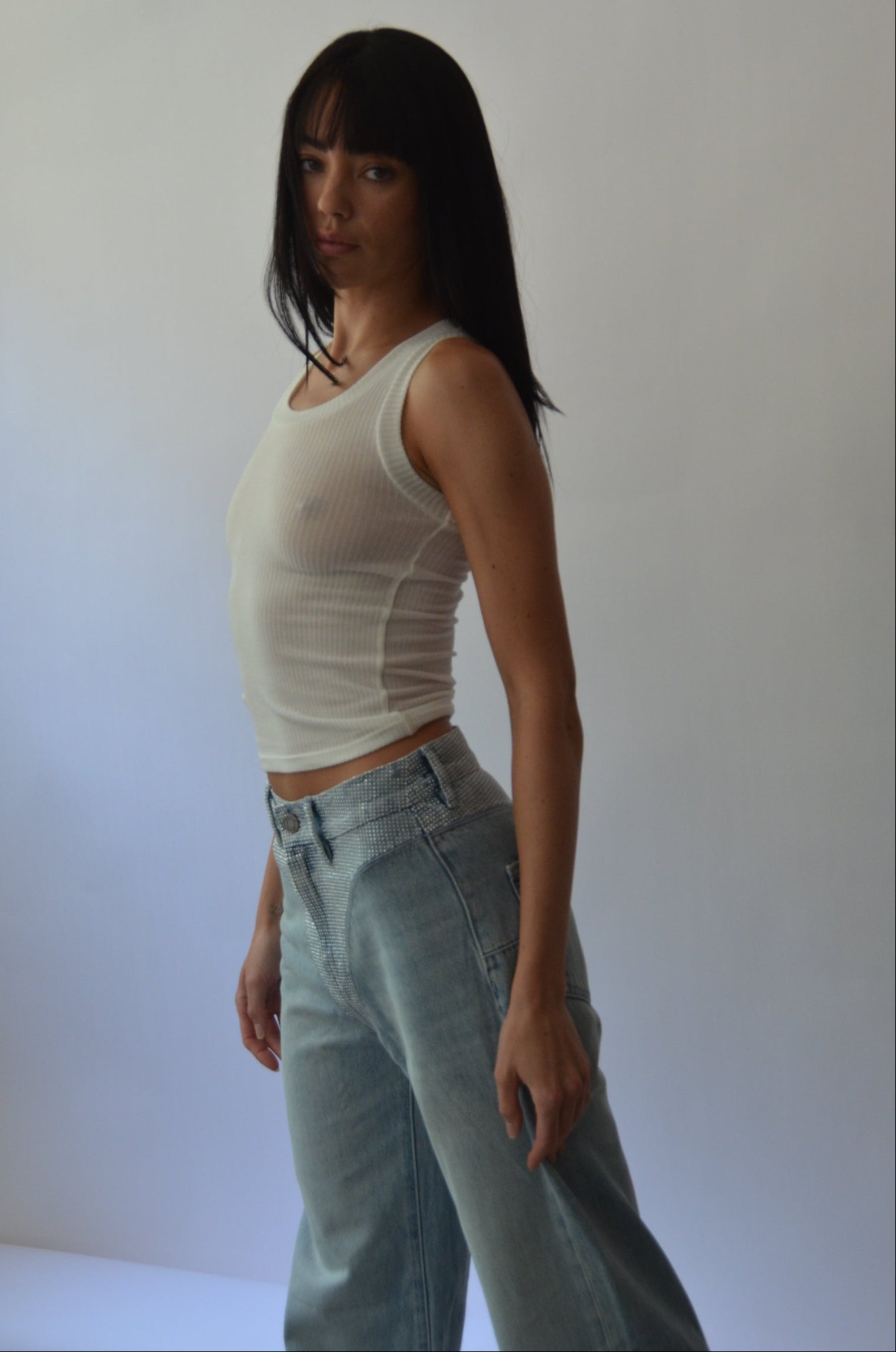 Person wearing a white sleeveless top and light blue jeans on a plain background