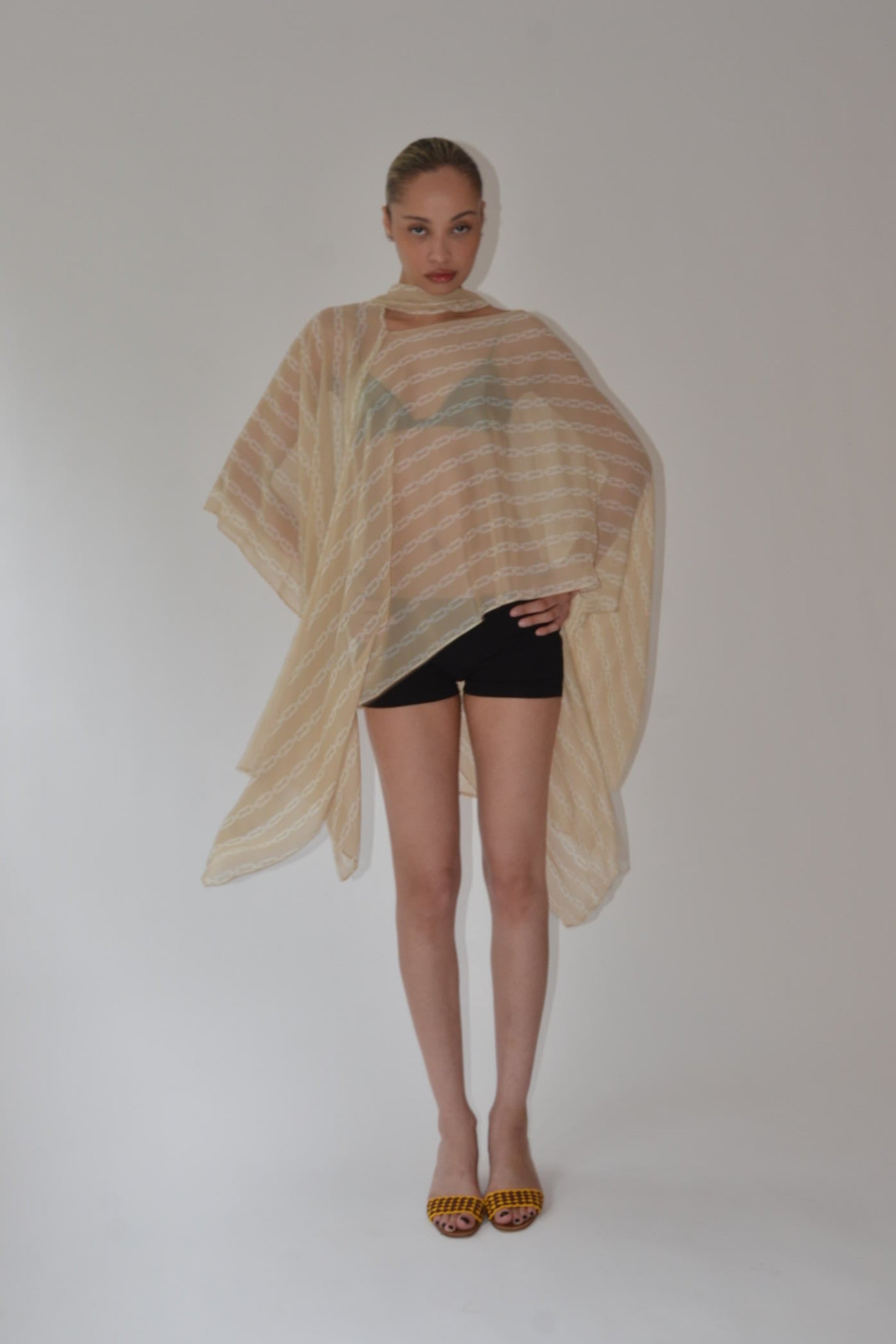 Person wearing a beige shawl over a black outfit on a white background