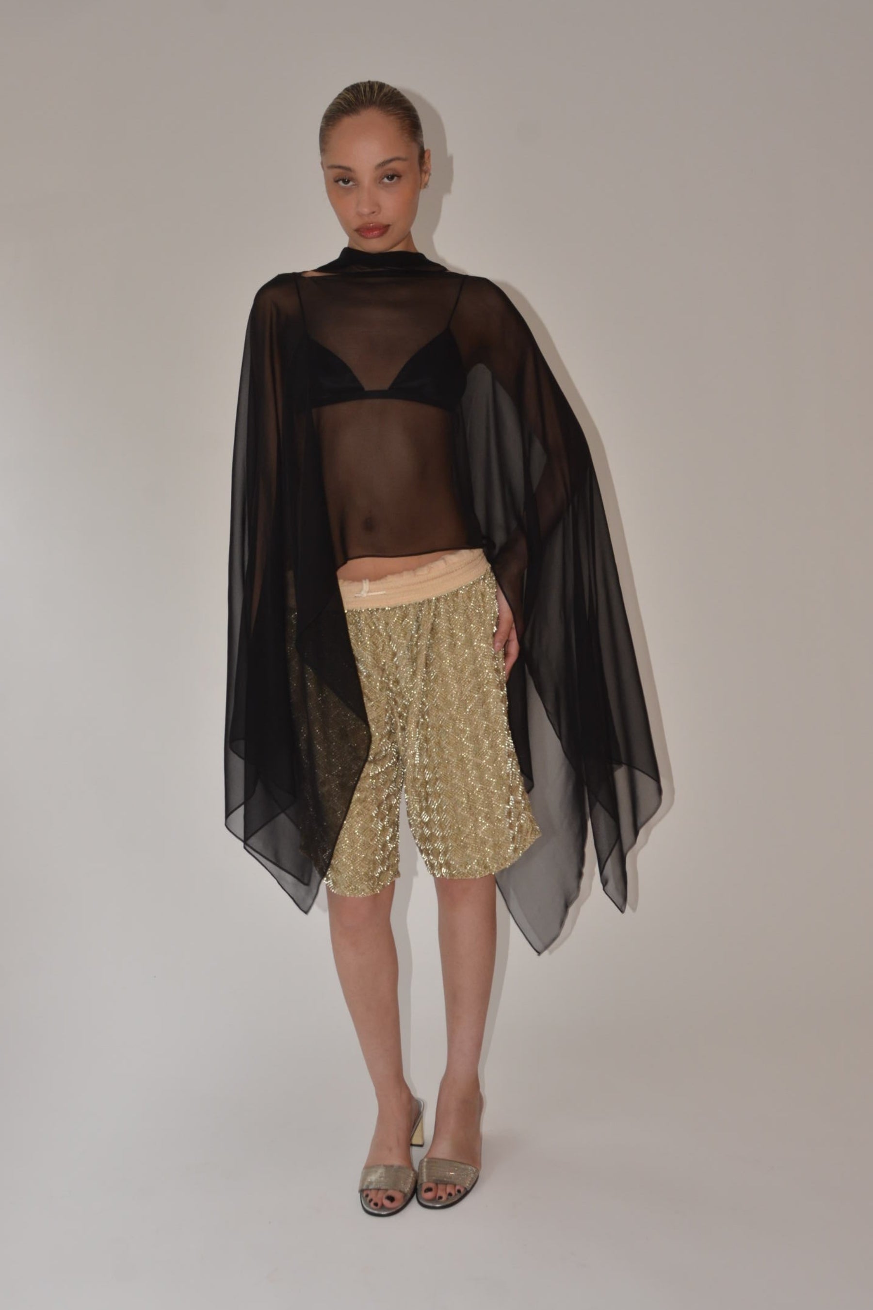 Person wearing a black sheer top and gold skirt on a white background