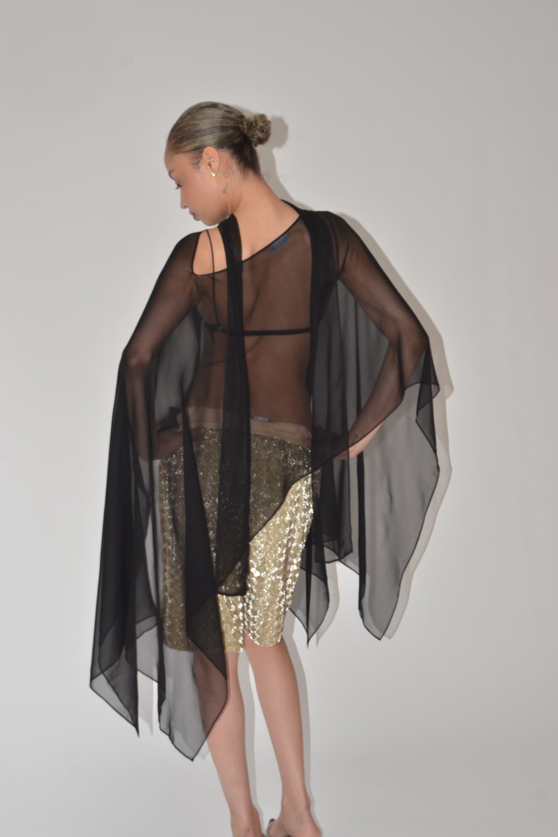 Person wearing a black sheer top with gold sequin skirt on a plain background