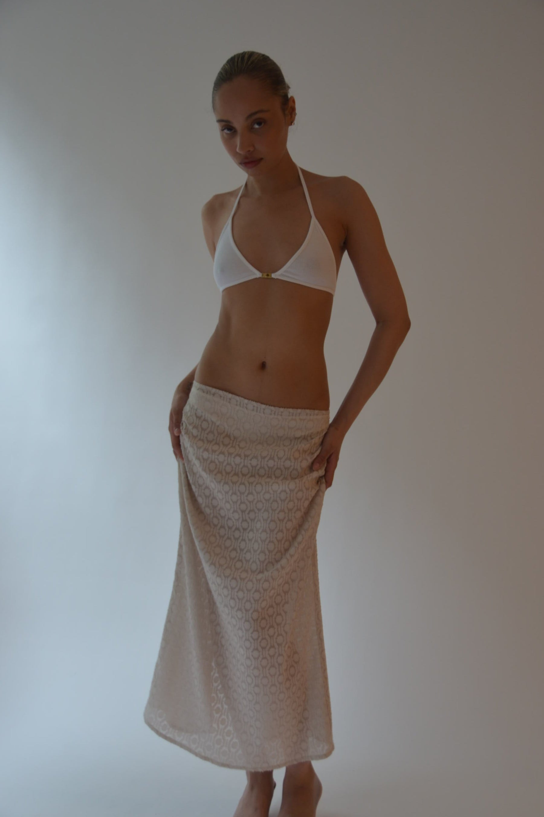 Woman wearing a white bikini and beige towel on a plain background