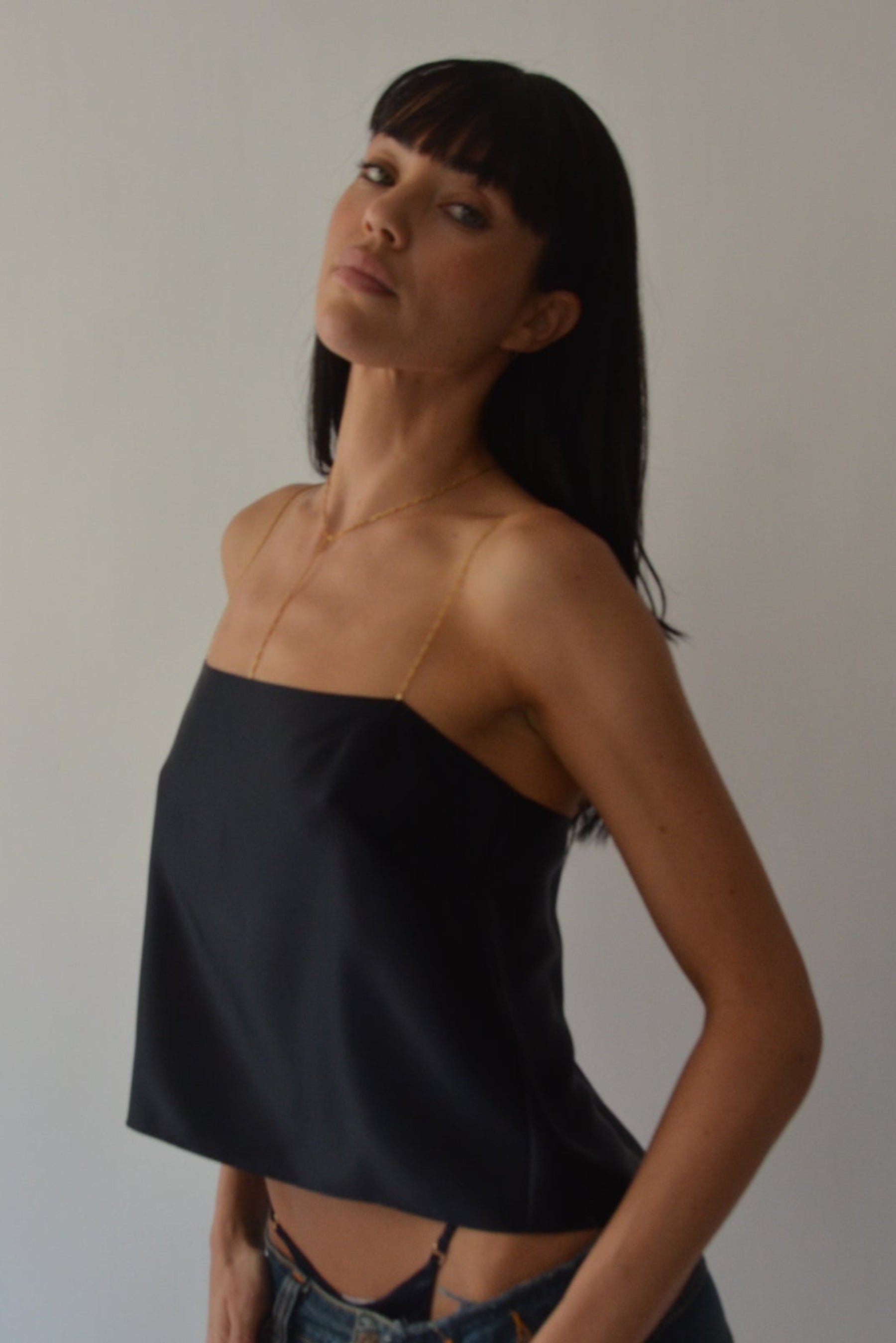 Woman wearing a navy silk top with chain straps against a plain background