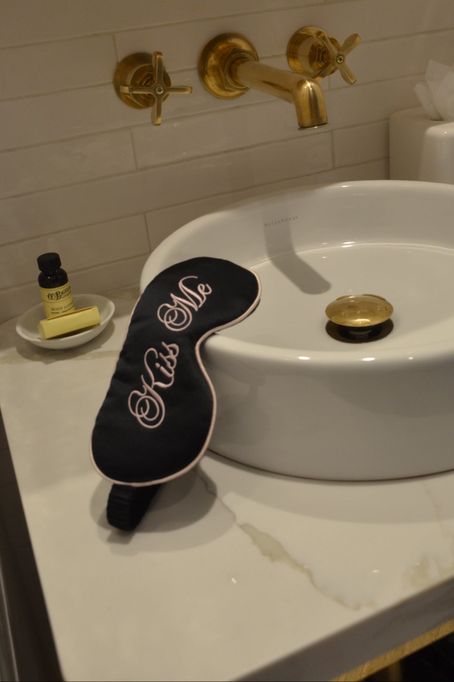 Black eye mask with &#39;Kiss Me&#39; text on a white sink in a bathroom setting.