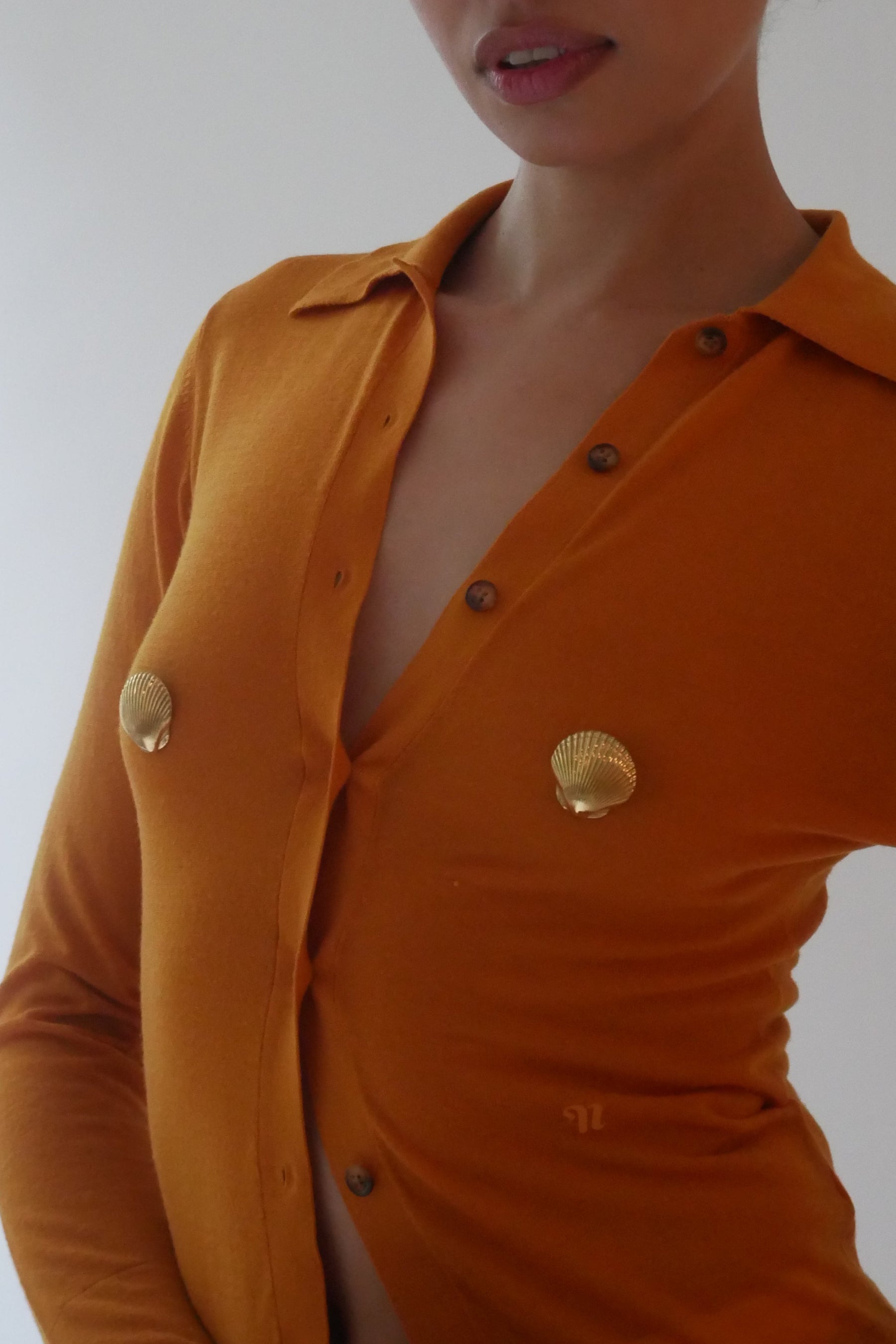 Person wearing an orange outfit with gold buttons against a plain background