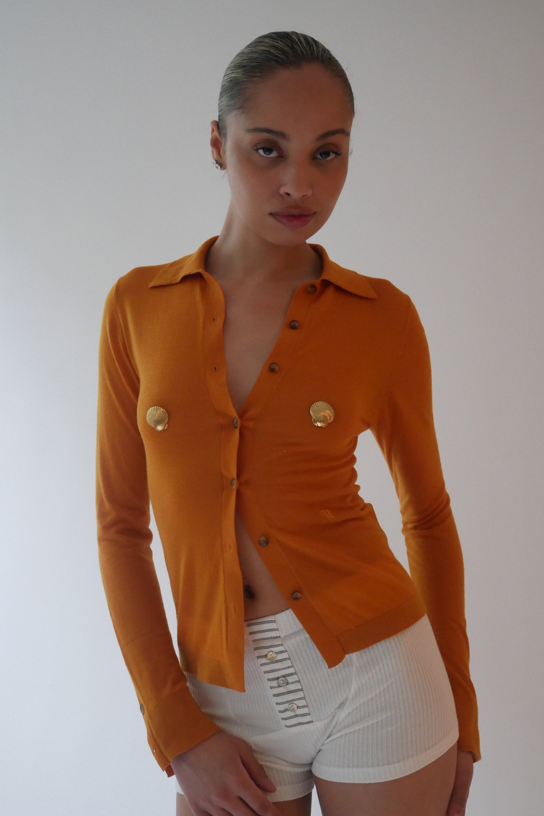 Person wearing an orange blazer with gold buttons on a plain background