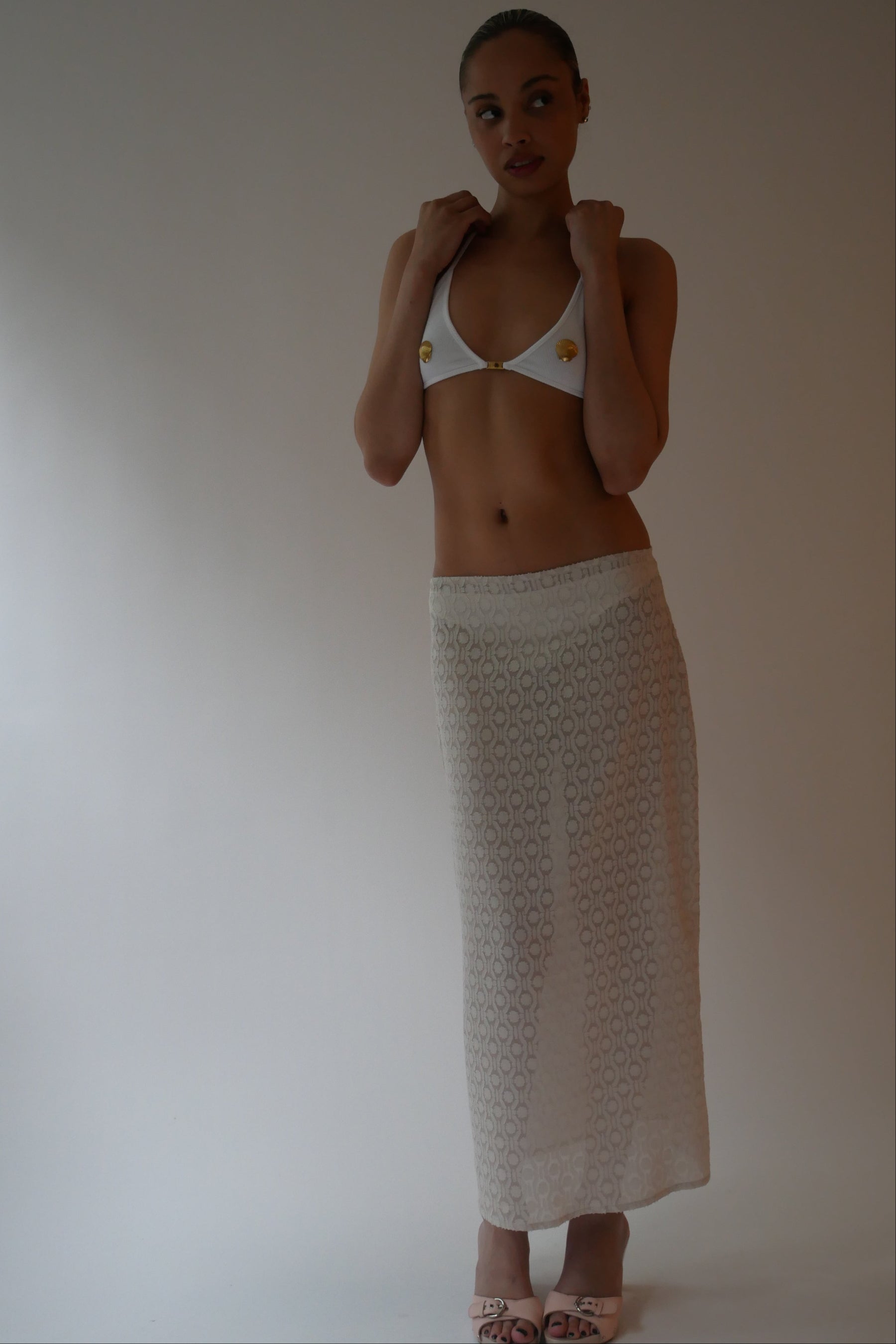 Woman wearing a white bikini top and skirt against a plain background