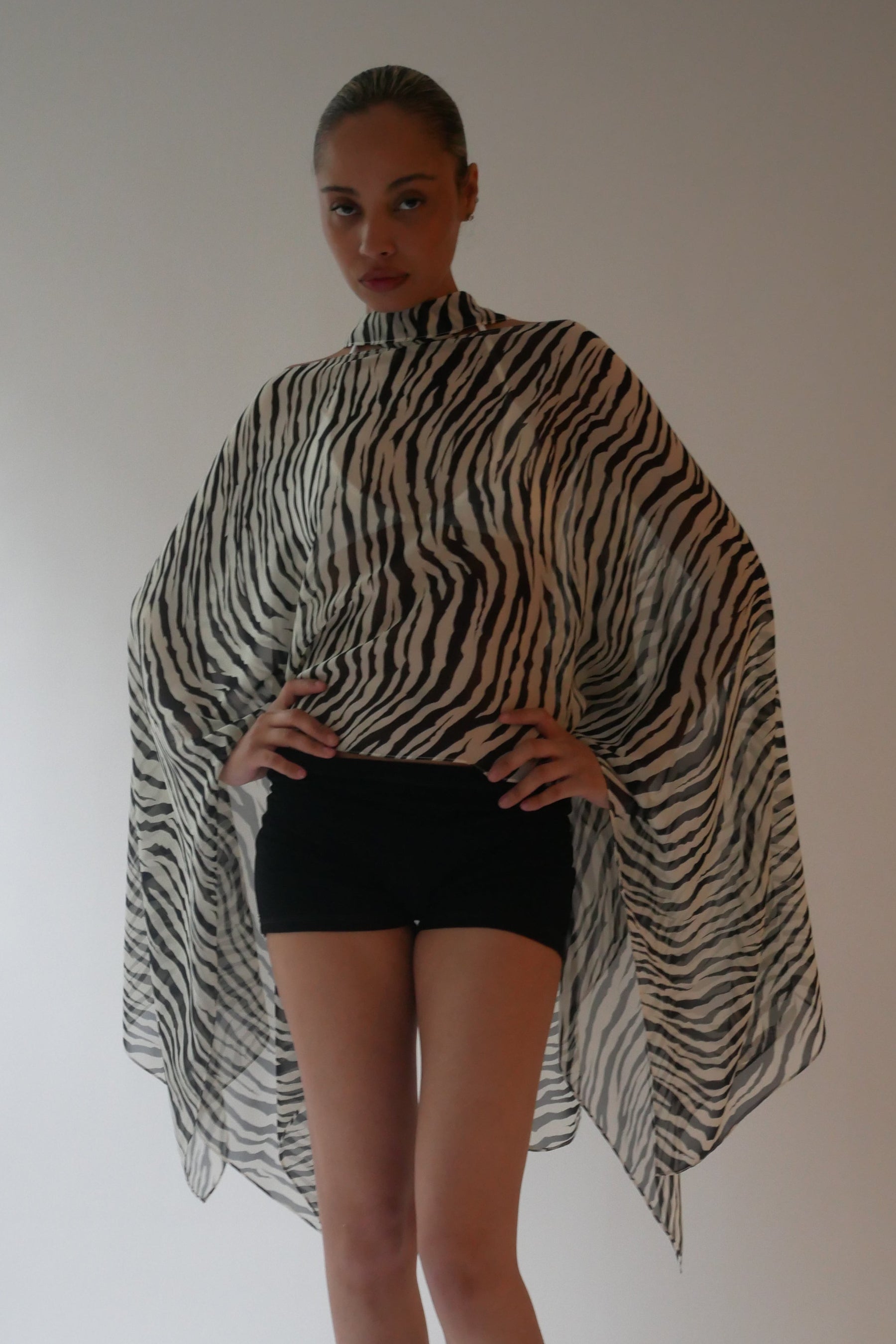 Person wearing a zebra print poncho over a black outfit against a plain background