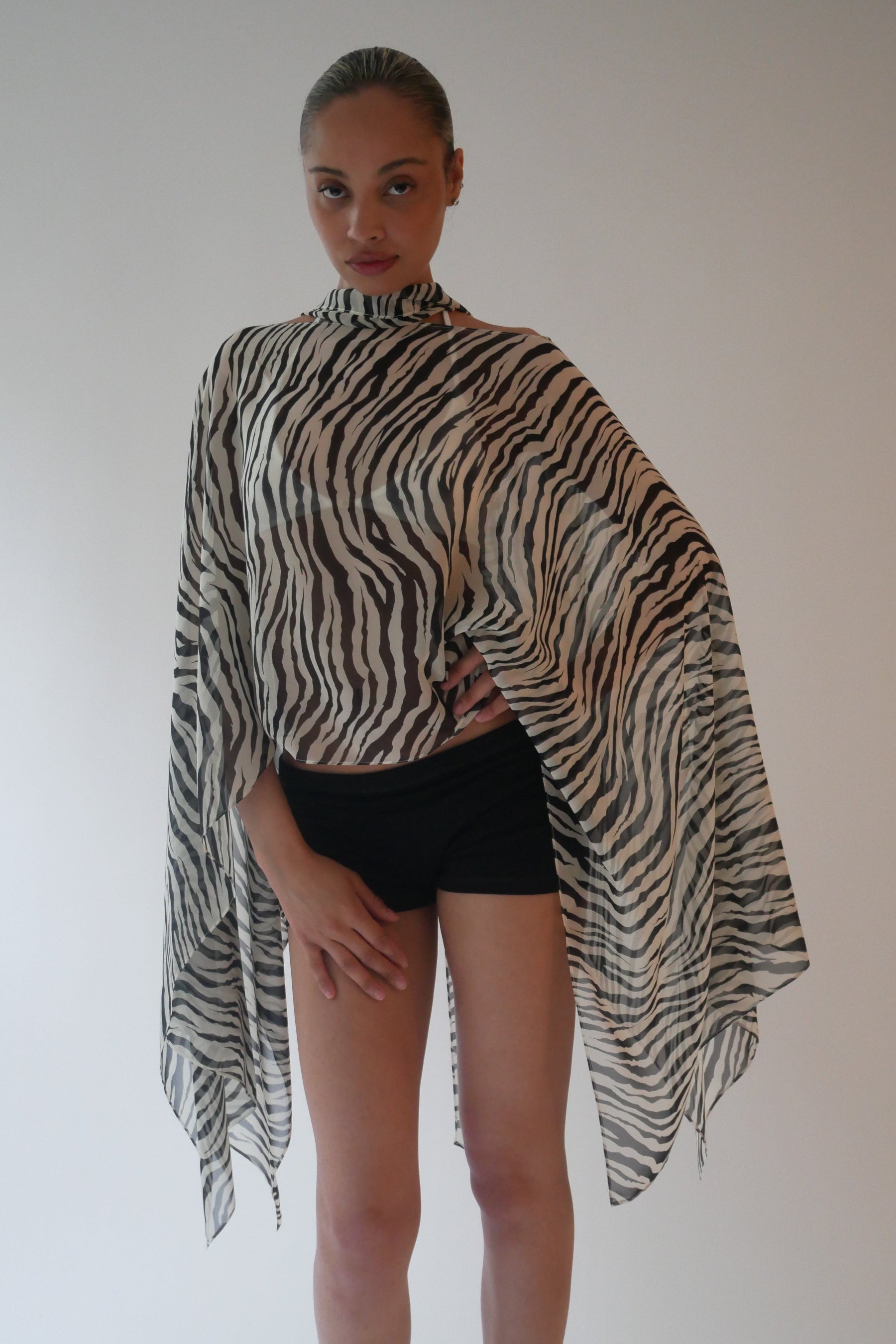 Person wearing a zebra print shawl over a black outfit against a plain background