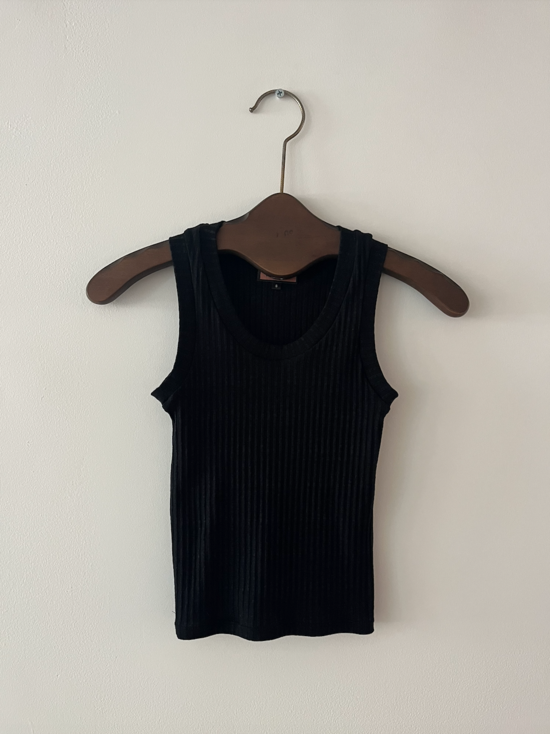 Black ribbed tank top on a wooden hanger against a white background